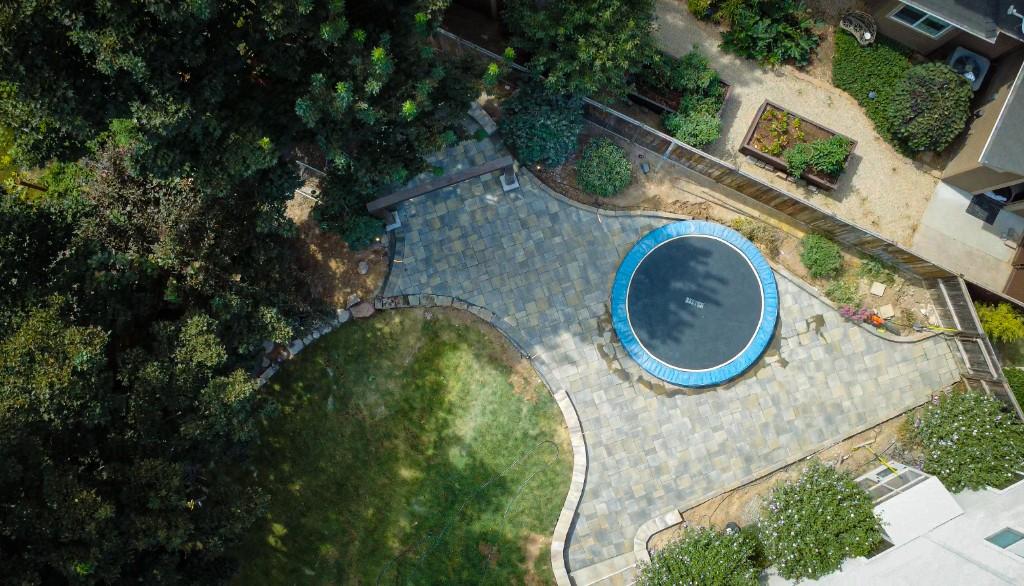 Paver patio around a trampoline with a wooden swing arch